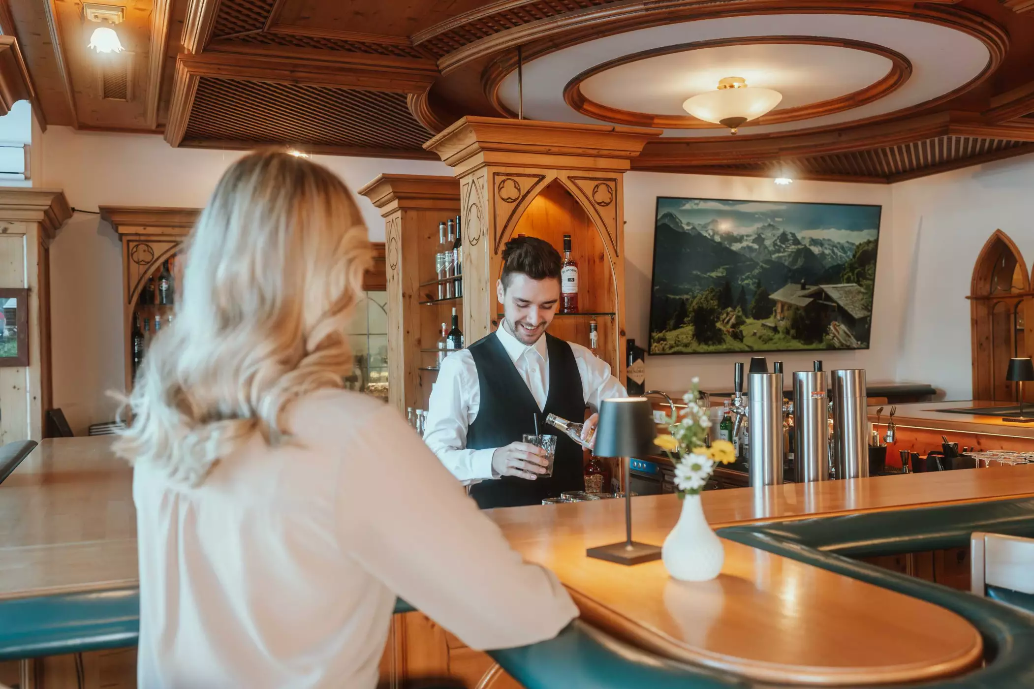 Restaurants in der Vitalquelle Montafoneingerichtete Weinstube mit Holzdecke, gemusterten Sitzpolstern, gedeckten Tischen mit weißen Tischdecken und Kerzen, dekorativen Figuren und einem großen Fass mit Blumengesteck.